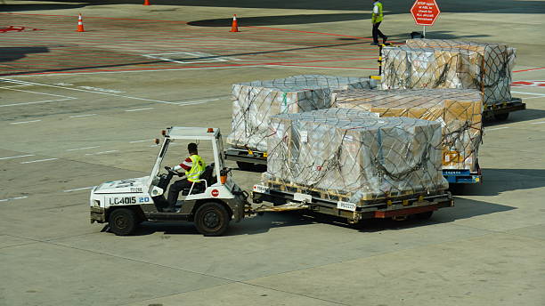 Nhân viên sân bay kéo các pallet hàng hóa thương mại bằng xe chuyên dụng, minh họa cho hoạt động gửi hàng thương mại đi Singapore.